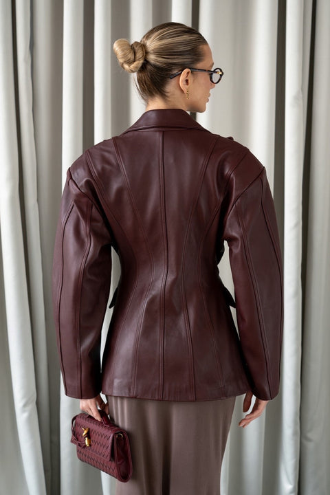 A woman wearing a refined burgundy leather blazer, tailored to accentuate the waist and crafted from supple leather for a chic, versatile look ideal for both professional and casual settings.