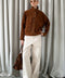 Elegant woman in cropped brown suede jacket, styled with wide-leg trousers and tortoiseshell sunglasses.