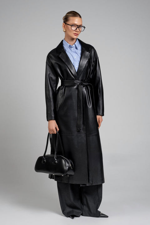 A woman wears a bold black leather coat with wide, structured shoulders, paired with wide trousers and a sleek black fashion leather bag, exuding modern power dressing.