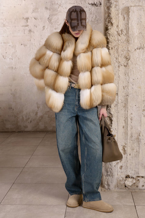 A woman pairs her denim jeans with a voluminous Gold Fox Fur Coat, the rich tones of the fur contrasting stylishly with her casual look.