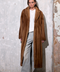 Model showcasing a Long Cognac Mink Fur Coat against a textured wall background.