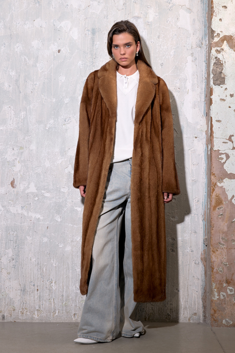 Model showcasing a Long Cognac Mink Fur Coat against a textured wall background.
